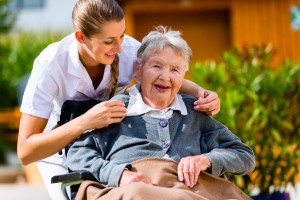 Senior woman in nursing home with nurse in garden sitting in wheelchair